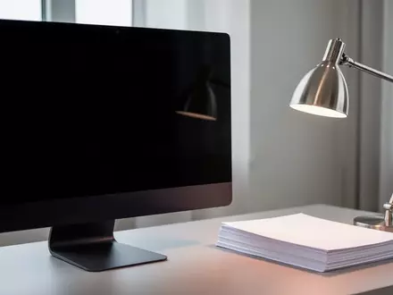Ein dunkler, minimalistischer Arbeitsplatz mit einem ausgeschalteten Monitor und einem Stapel leerer Dokumente. - Foto: ĂĽber boerse-global.de