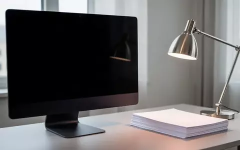 Ein dunkler, minimalistischer Arbeitsplatz mit einem ausgeschalteten Monitor und einem Stapel leerer Dokumente. - Foto: über boerse-global.de