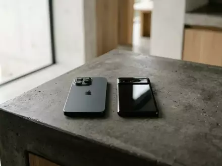 Zwei moderne Smartphones liegen nebeneinander auf einer minimalistischen Betonoberfläche in natürlichem Licht. - Foto: über boerse-global.de