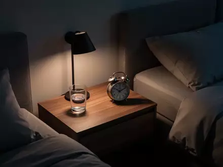 Ein minimalistisches, modern eingerichtetes Schlafzimmer bei Nacht mit warmem, gedimmtem Licht und einem Nachttisch. - Foto: über boerse-global.de