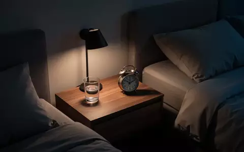 Ein minimalistisches, modern eingerichtetes Schlafzimmer bei Nacht mit warmem, gedimmtem Licht und einem Nachttisch. - Foto: über boerse-global.de