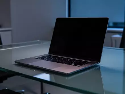 Ein moderner, dunkel beleuchteter Büroarbeitsplatz mit einem Laptop auf einem minimalistischen Schreibtisch. - Foto: über boerse-global.de