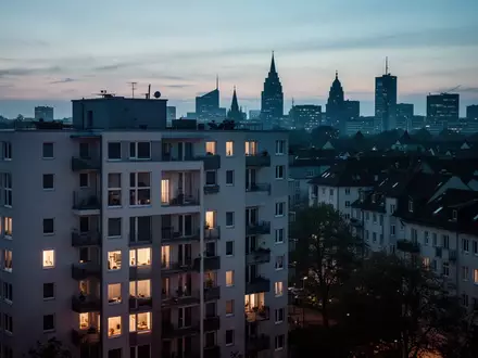 Ein modernes Wohngebäude in einem dicht besiedelten Stadtgebiet bei Dämmerung mit warm beleuchteten Fenstern. - Foto: über boerse-global.de