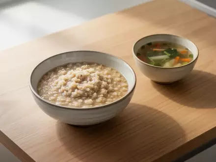 Eine Schale mit Porridge und eine Schale mit klarer Suppe auf einem minimalistischen Holztisch bei natürlichem Licht. - Foto: über boerse-global.de