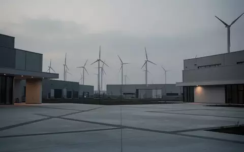 Moderne Industrieanlage bei Dämmerung mit ungenutzten Windkraftanlagen im Hintergrund. - Foto: über boerse-global.de