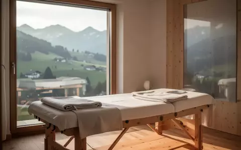 Minimalistische, lichtdurchflutete Therapieräumlichkeit mit Massageliege vor einem Fenster mit Blick auf die Appenzeller Hügel. - Foto: über boerse-global.de