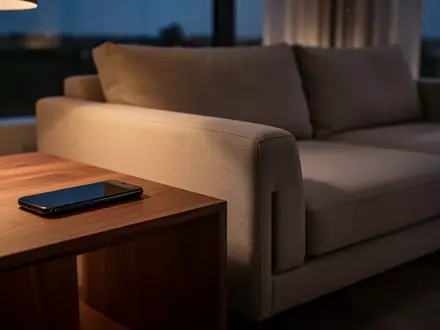 Ein ausgeschaltetes Smartphone auf einem Holztisch in einem gemütlich beleuchteten Wohnzimmer am Abend. - Foto: über boerse-global.de