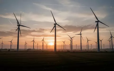 Ein moderner Windpark bei Sonnenuntergang in einer weiten Landschaft, der kritische Energieinfrastruktur symbolisiert. - Foto: über boerse-global.de