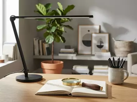 Eine moderne, minimalistische Schreibtischleuchte und eine hochwertige Lupe auf einem sauberen Schreibtisch in einem hellen, wohnlichen Büro. - Foto: über boerse-global.de