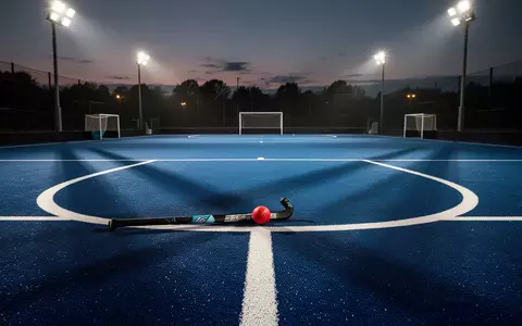 Ein unbespieltes Hockeyfeld bei Dämmerung mit einem einzelnen Ball im Schusskreis unter Flutlicht. - Foto: über boerse-global.de