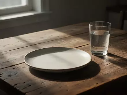 Ein leerer Teller und ein Glas Wasser auf einem schlichten Holztisch bei natürlichem Licht, symbolisch für finanzielle Sorgen. - Foto: über boerse-global.de