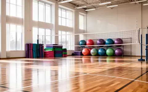 Leere, helle Sporthalle mit Sportgeräten wie Gymnastikbällen und einem Volleyballnetz im Hintergrund. - Foto: über boerse-global.de