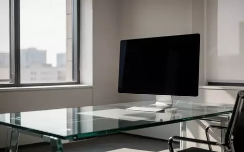 Ein moderner, minimalistischer Büroarbeitsplatz mit einem ausgeschalteten Monitor vor einem großen Fenster. - Foto: über boerse-global.de