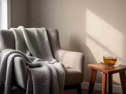 Ein ruhiger, minimalistischer Raum mit einem bequemen Sessel, einer Decke und einer Tasse Tee bei natürlichem Tageslicht. - Foto: über boerse-global.de