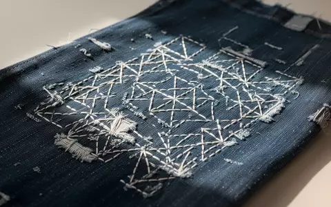 Nahaufnahme von indigoblauem Denim mit kunstvollen weißen Sashiko-Stickereien als sichtbare Reparaturmaßnahme. - Foto: über boerse-global.de