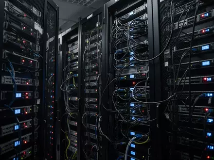 Dunkler Serverraum mit leuchtenden Hardware-Racks und komplexer Verkabelung als Symbol für Cyber-Sicherheitsbedrohungen. - Foto: über boerse-global.de
