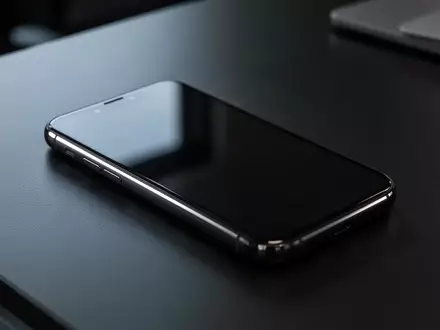 Ein dunkles Smartphone liegt auf einem Schreibtisch; der Bildschirm ist ausgeschaltet und reflektiert das Umgebungslicht. - Foto: über boerse-global.de