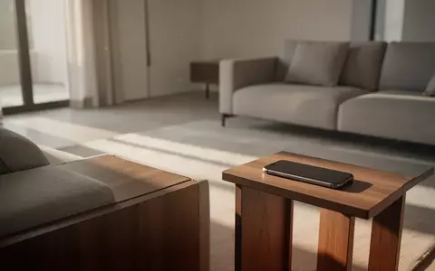 Ein Smartphone liegt verdeckt auf einem Holztisch in einem modernen, hellen Wohnzimmer. - Foto: über boerse-global.de