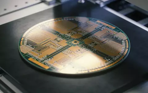 Ein Silizium-Wafer mit Mikrochip-Strukturen liegt auf einer dunklen Werkbank in einer Fertigungshalle. - Foto: über boerse-global.de