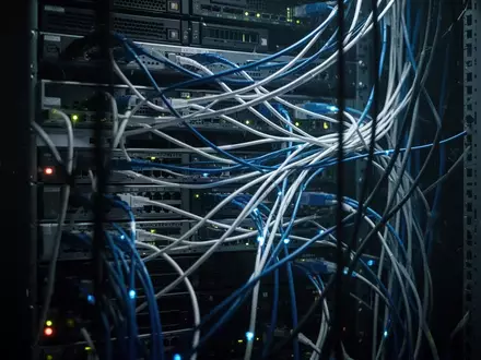 Ein technischer Serverraum mit leuchtenden Glasfaserkabeln in einer düsteren, angespannten Atmosphäre. - Foto: über boerse-global.de
