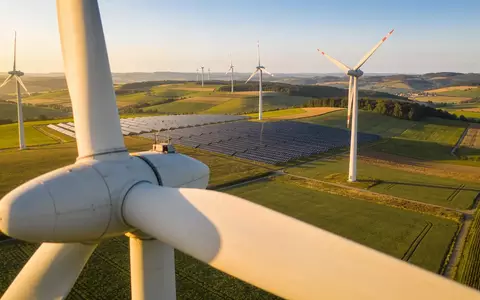 Weite ländliche Landschaft mit Windkraftanlagen und Solarpaneelen in landwirtschaftlichen Feldern bei goldenem Licht. - Foto: über boerse-global.de