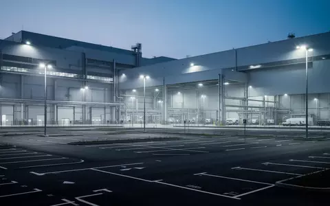 Ein weitläufiges, modernes Automobilwerk in der Dämmerung mit leeren Parkplätzen und industrieller Beleuchtung. - Foto: über boerse-global.de
