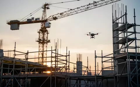 Eine Baustelle mit Gerüsten und einem Baukran bei Sonnenuntergang, ergänzt durch eine Drohne für Bauinspektionen. - Foto: über boerse-global.de