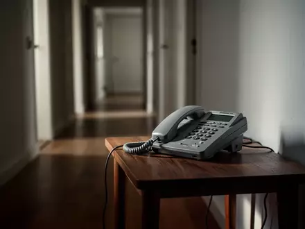 Ein klassisches Festnetztelefon auf einem Holztisch in einem flurartigen Wohnbereich. - Foto: über boerse-global.de