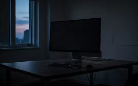 Ein dunkler, minimalistischer Arbeitsplatz mit einem ausgeschalteten Computerbildschirm in einem schattigen Raum. - Foto: über boerse-global.de