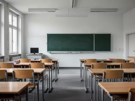 Ein leerer Klassenraum in einer Schule mit Holztischen und einer Schultafel bei Tageslicht. - Foto: über boerse-global.de