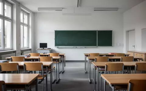 Ein leerer Klassenraum in einer Schule mit Holztischen und einer Schultafel bei Tageslicht. - Foto: über boerse-global.de