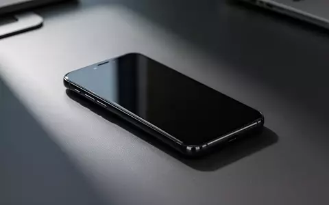 Ein ausgeschaltetes Smartphone liegt auf einem dunklen Schreibtisch in einer modernen Büroumgebung. - Foto: über boerse-global.de