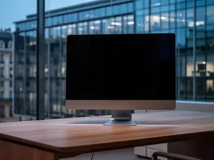 Ein dunkler, moderner Büroarbeitsplatz mit einem ausgeschalteten Computerbildschirm vor einer gläsernen Fassade. - Foto: über boerse-global.de