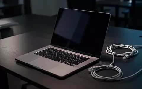 Ein Laptop auf einem dunklen Büroschreibtisch mit einem daneben liegenden Ethernet-Kabel in einer schattigen Umgebung. - Foto: über boerse-global.de