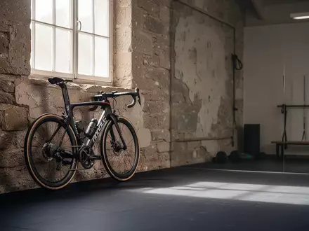 Ein Rennrad lehnt an einer Wand in einem leeren Trainingsraum, symbolisch für die Suche nach körperlicher Auslastung. - Foto: über boerse-global.de