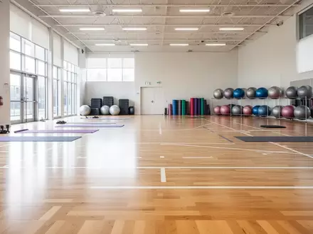 Helle, moderne Sporthalle mit aufgeräumten Trainingsgeräten wie Yogamatten und Gymnastikbällen auf einem Holzboden. - Foto: über boerse-global.de