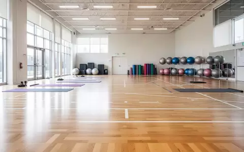 Helle, moderne Sporthalle mit aufgeräumten Trainingsgeräten wie Yogamatten und Gymnastikbällen auf einem Holzboden. - Foto: über boerse-global.de