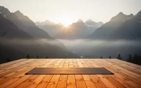 Leere Holzplattform für Yoga vor einer alpinen Bergkulisse im sanften Licht des frühen Morgens. - Foto: über boerse-global.de