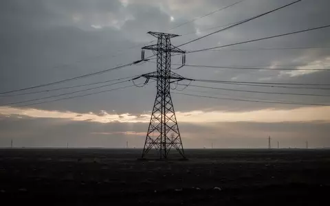 Ein Hochspannungsmast auf einem weiten Feld unter einem bewölkten Himmel bei Dämmerung. - Foto: über boerse-global.de