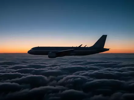 Ein Passagierflugzeug fliegt in der Dämmerung über einer dichten Wolkendecke. - Foto: über boerse-global.de