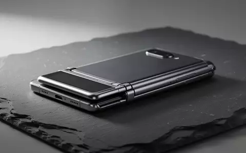 Ein minimalistisches, teilweise zusammengefaltetes Smartphone in einem hochwertigen, metallischen Design auf einer dunklen Schieferoberfläche. - Foto: über boerse-global.de