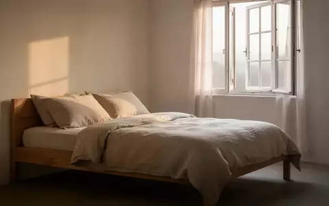 Ein minimalistisch eingerichtetes, helles Schlafzimmer mit natĂĽrlichem Tageslicht und ordentlich bezogenem Bett. - Foto: ĂĽber boerse-global.de