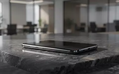 Ein minimalistisches Smartphone liegt auf einer dunklen Steinoberfläche vor einem unscharfen büroähnlichen Hintergrund. - Foto: über boerse-global.de