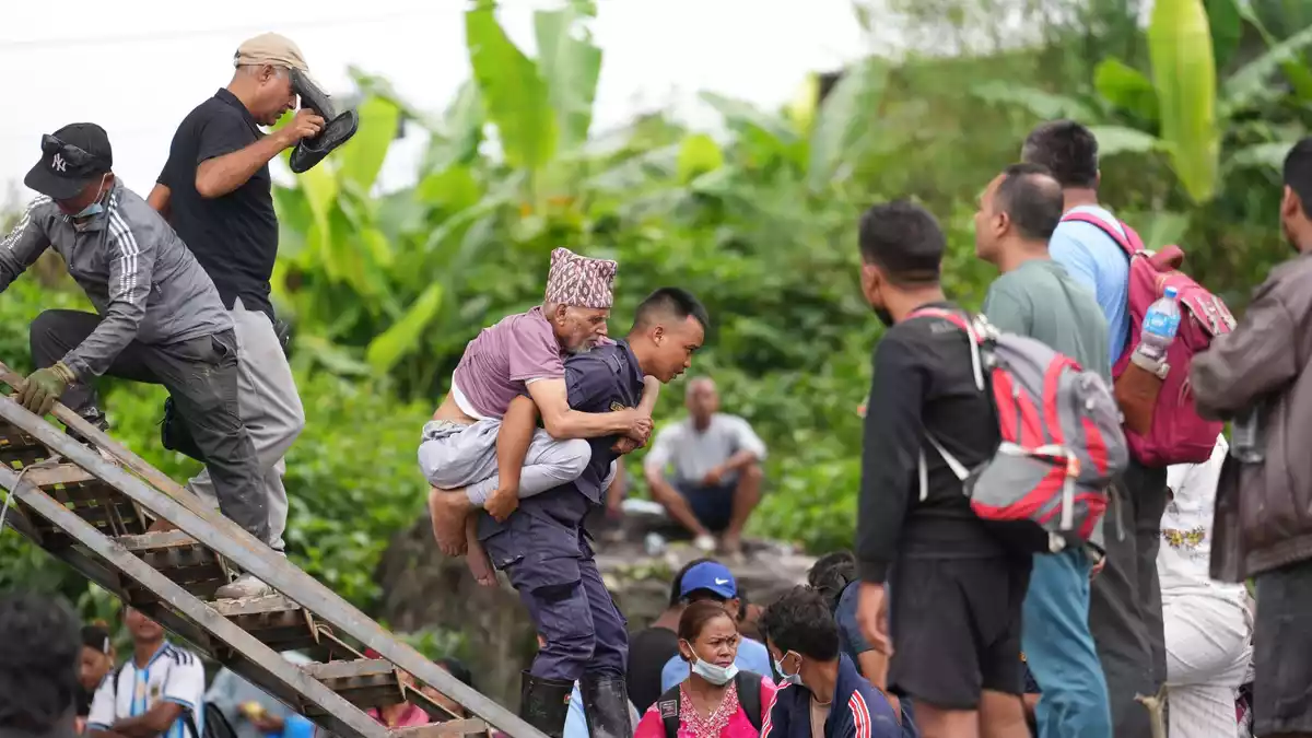 Ein Mann wird im Katastrophengebiet in Nepal von einem Polizisten auf dem Rücken getragen. - Bild: Rajesh Kumar Singh/AP/dpa