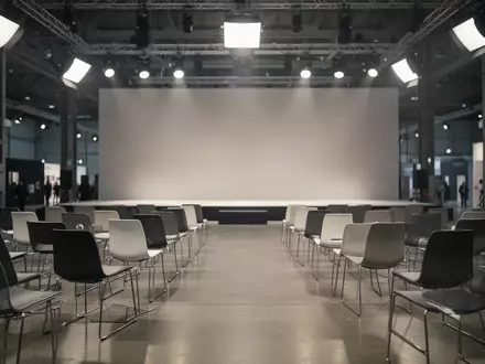 Ein minimalistischer, leerer Veranstaltungsraum auf einer Messe in Berlin mit moderner Architektur und indirekter Beleuchtung. - Foto: über boerse-global.de