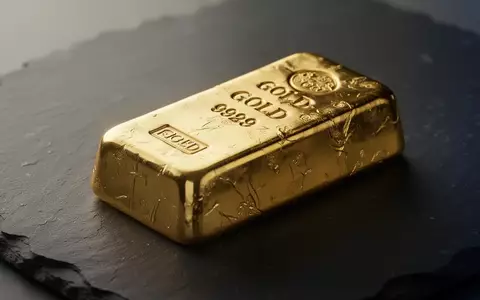 Ein goldener Barren liegt auf einer dunklen, texturierten Oberfläche bei weichem Licht. - Foto: über boerse-global.de