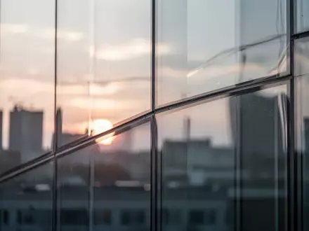 Moderne, minimalistische Glasfassade mit fließenden, transparenten Reflexionen bei Sonnenuntergang. - Foto: über boerse-global.de