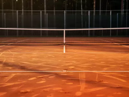 Ein leerer Tennisplatz aus rotem Sand in der Abendsonne, der auf ein professionelles Training in einer ruhigen Umgebung hindeutet. - Foto: über boerse-global.de