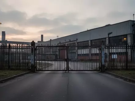 Ein Fabrikgelände mit einem großen Produktionsgebäude und einem Metallzaun bei Dämmerung. - Foto: über boerse-global.de