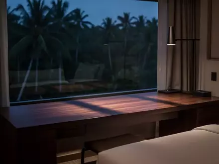 Ein minimalistisch eingerichtetes Hotelzimmer bei Dämmerung mit einem leeren Schreibtisch und Blick auf eine tropische Landschaft. - Foto: über boerse-global.de